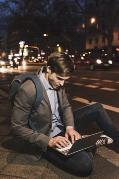 Businessman using laptop on urban street at night