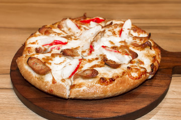 Fast food italian traditional.Hot chicken sausage pizza with cheese, imitation crab stick on wooden board table classic in top view.Closed up.Copy space.