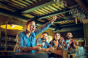 Sport, people, leisure, friendship and entertainment concept - happy football fans or male friends drinking beer and celebrating victory at bar or pub