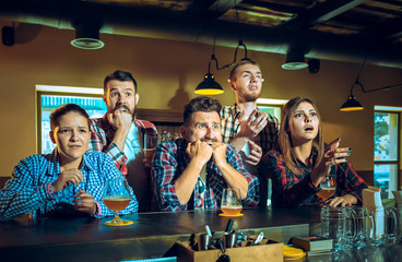 Sport, people, leisure, friendship and entertainment concept - happy football fans or male friends drinking beer and celebrating victory at bar or pub