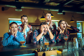 Sport, people, leisure, friendship and entertainment concept - happy football fans or male friends drinking beer and celebrating victory at bar or pub