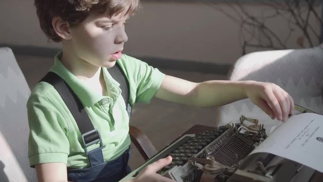 Pleased little six-year-old boy studies the work of an old typewriter.