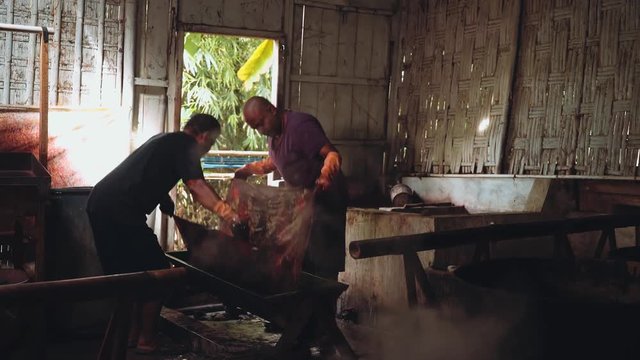 Two indonesian men dyeing batik fabric in dark workshop shed in Pekalongan, Indonesia