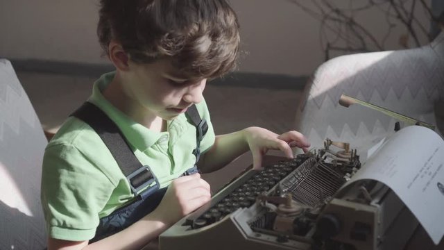 Pleased little six-year-old boy studies the work of an old typewriter.