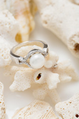 Silver ring with pearl and diamonds on coral against white background