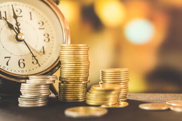 money and time concept with stack of coin and clock on table over blur gold background 