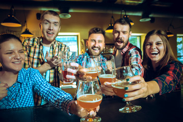 Sport, people, leisure, friendship and entertainment concept - happy football fans or male friends drinking beer and celebrating victory at bar or pub