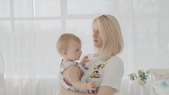 Mother swinging her beautiful daughter in the room. Young mom kissing her baby. Happy family. Slow motion
