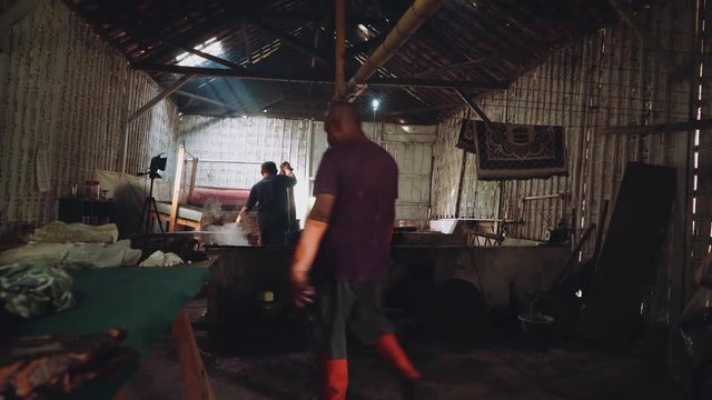 Two indonesian men walking in dark workshop shed with batik fabric in Pekalongan, Indonesia
