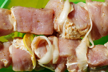 pieces of raw shish kebab meat on skewer with onion and lemon