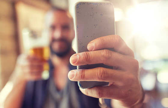 people, leisure and technology concept - close up of man with smartphone drinking beer and taking selfie at bar or pub