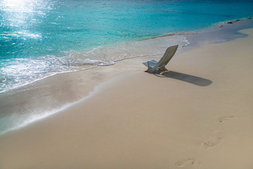 Fototapeta na wymiar Lone chaise longue on clean sand near the ocean shore
