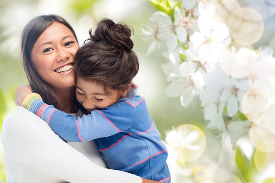family, motherhood and people concept - happy mother and daughter hugging over cherry blossom background