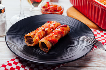 Italian cannelloni stuffed with minced meat and served with tomato sauce and red wine on black plates.