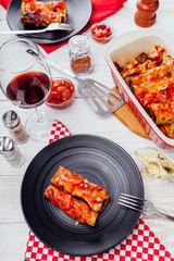 Italian cannelloni stuffed with minced meat and served with tomato sauce on black plates. Dinner for two