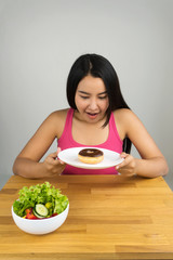Obraz na płótnie Canvas beautiful young Asian woman choosing chocolate doughnut and ignoring salad bowl