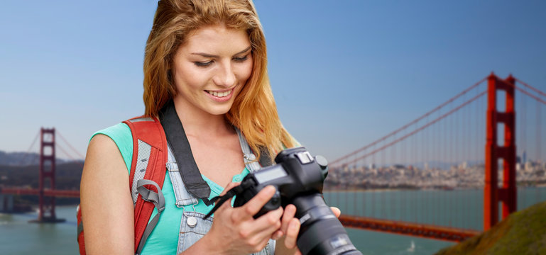 travel, tourism and photography concept - happy young woman with backpack and camera photographing over golden gate bridge in san francisco bay background