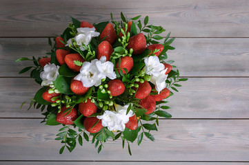 Bouquet from flowers and fruit. Ripe strawberry and white freesia. Wooden background. Top view