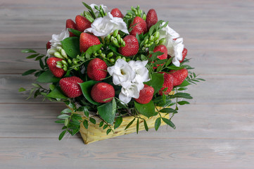 Bouquet from flowers and fruit. Ripe strawberry and white freesia. Wooden background