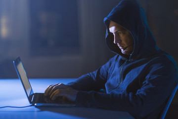 cybercrime, hacking and technology concept - male hacker with microphone using laptop computer for...