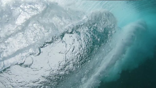 SLOW MOTION, CLOSE UP, LOW ANGLE, UNDERWATER: Joyful surfboarder drags his hand behind him as he rides an ocean wave on sunny day in the picturesque seaside. Athletic man surfing in beautiful Pacific.