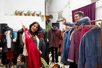 sale, shopping, fashion and people concept - happy couple choosing clothes at vintage clothing store and showing thumbs up