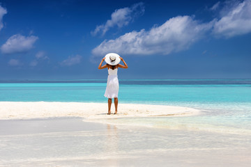 Attraktive Frau in weißem Kleid steht an einem tropischen Strand mit türkisem Meer und weißen...