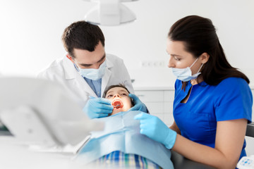 Obraz na płótnie Canvas medicine, dentistry and healthcare concept - dentist with mouth mirror checking for kid patient teeth at dental clinic