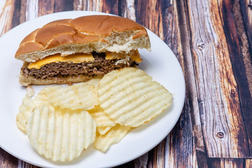 Half homemade cheeseburger with chips on white plate and wood table background