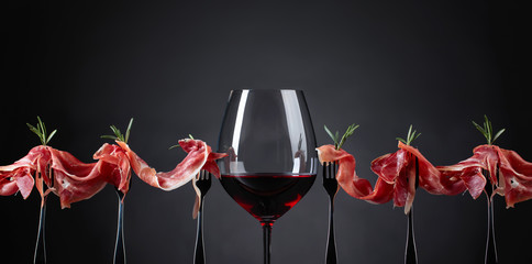 Prosciutto with rosemary and glass of red wine on a dark background.