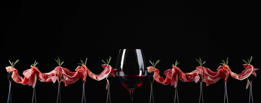 Prosciutto with rosemary and glass of red wine on a black background.