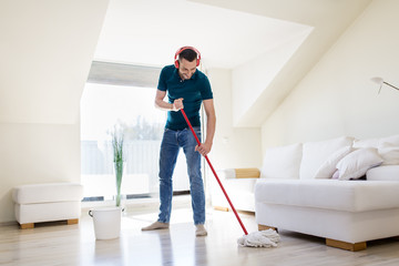 people, housework and housekeeping concept - happy man in headphones with mop cleaning floor at home