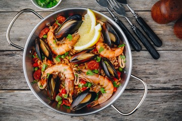 Spanish seafood paella with mussels, shrimps and chorizo sausages in traditional pan on wooden background.
