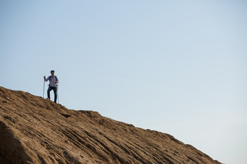 Photo of sportsman with backpack and walking sticks on hill