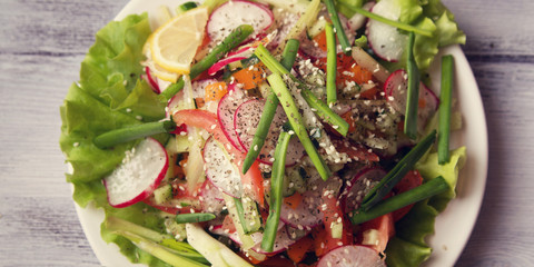 Spring Vegetable Salad on the white plate. Radish, tomato, celery and cucumber. Topped with sesame seeds. Vegetarian dish on the white wooden table. Close up. Top view. Wide photo.