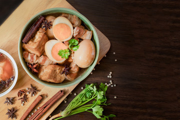 Eggs and sweet pork with fried tofu, boiled in brown sauce and in white bowl on old brown wooden plank and space for messages and texts.Thai food called Pha-lo.