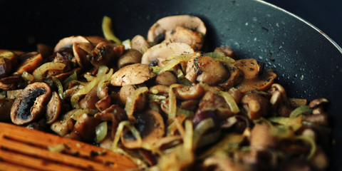 A skillet with a fried mushrooms. Vegan dish. Fried mushrooms and onion in the frying pan. European cuisine. Pan fried mushrooms. Simple vegetarian meal. Wide photo. Close up. Selective focus.