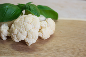 Cauliflower and basil leaves on a wooden background. Close-up. Copy space.
