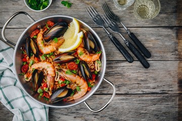 Spanish seafood paella with mussels, shrimps and chorizo sausages in traditional pan on wooden background.