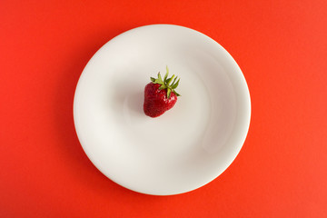 One strawberry in the white  plate  on the red  background.Top view.Diet minimal concept.