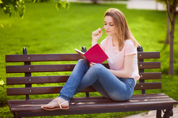 Girl reading a notebook sitting on a bench in the Park