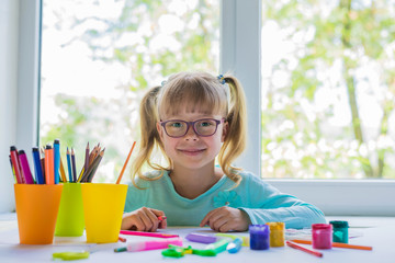 Cute little girl doing homework, reading a book, coloring pages, writing and painting. Children paint. Kids draw. Preschooler with books at home. Preschoolers learn to write and read. Creative toddler