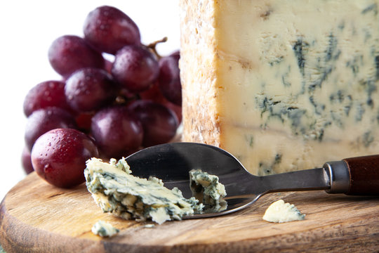Stilton on a cheese board with red grapes and cheese spoon