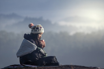 Girl relaxing on the hill sitting in a sleeping bag and drinking hot drink, enjoying holidays, travel and people concept. Sun glare effect