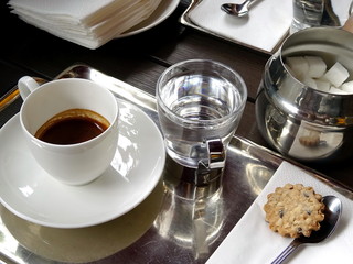 A cup of espresso, a glass of water, a cookie on a tray