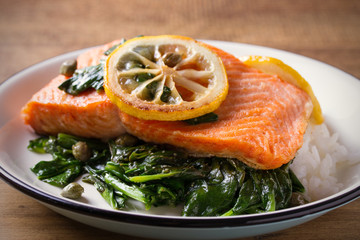 Salmon fillet with rice and spinach garnish. Fish steak. Lemon salmon on white plate on wooden background. horizontal