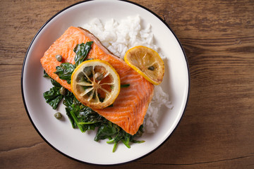 Salmon fillet with rice and spinach garnish. Fish steak. Lemon salmon on white plate on wooden background. overhead, horizontal