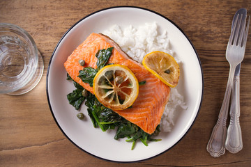 Salmon fillet with rice and spinach garnish. Fish steak. Lemon salmon on white plate on wooden background. overhead, horizontal