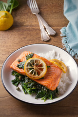Salmon fillet with rice and spinach garnish. Fish steak. Lemon salmon on white plate on wooden background. overhead, horizontal