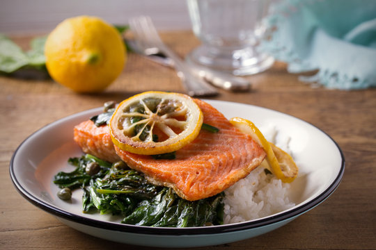 Salmon fillet with rice and spinach garnish. Fish steak. Lemon salmon on white plate on wooden background. horizontal